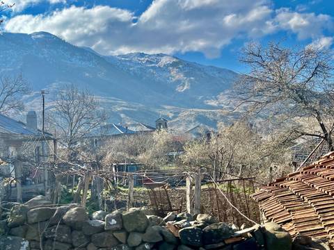 Rustic mountain village with orchards and snow-capped peaks under a blue sky.