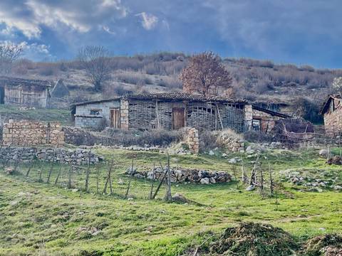Rural hillside with stone fences and old wattle farmhouse amid winter-brown shrubs and grass.