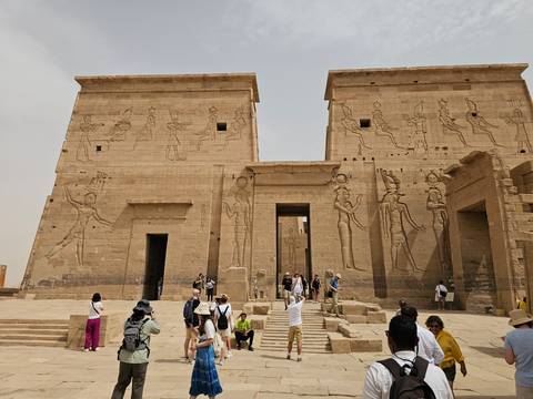 Visitors exploring the twin pylons and columns of Philae Temple complex under a pale sky.