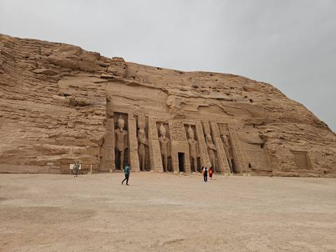 Rock-cut Small Temple at Abu Simbel with colossal standing figures carved into the cliff face and a few visitors below.