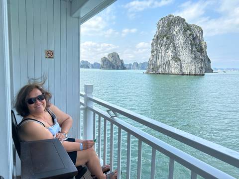 Woman relaxing on a cruise balcony overlooking emerald waters and limestone islands.