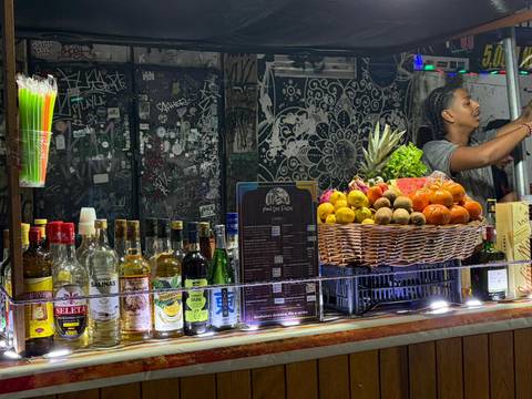 Colorful bar stall displaying fresh fruit and liquor bottles with a bartender preparing drinks.