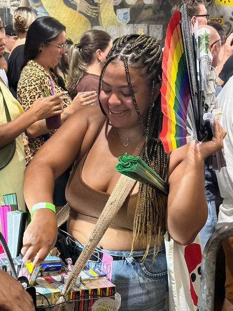 Woman selecting items at a lively indoor market, holding a rainbow fan.