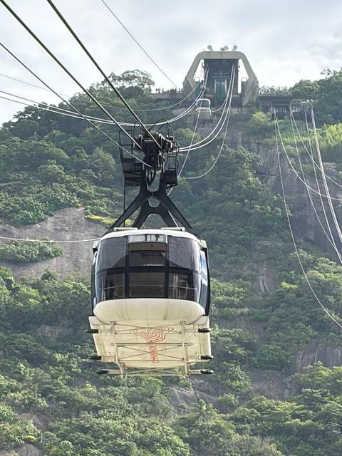 Sugarloaf cable car ascending against a backdrop of green cliffs and hanging cables.