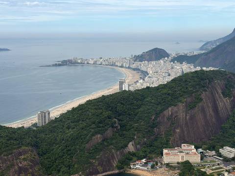 Expansive aerial of Copacabana Beach curving along the coast beneath forested cliffs.