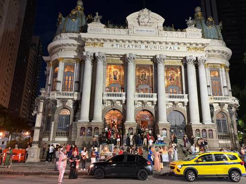 Nighttime crowd gathered outside the illuminated neoclassical façade of Rio's Theatro Municipal.