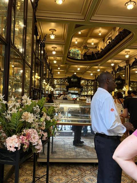 Elegant interior of a historic café with glass showcases and ornate mirrors bustling with patrons.