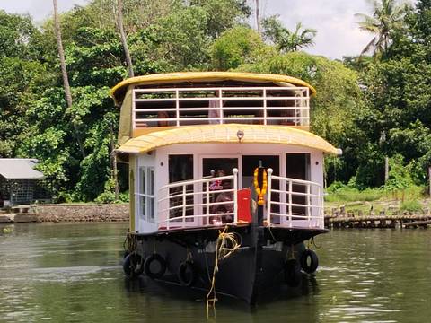 Traditional Kerala houseboat with yellow thatched roof cruising along tranquil backwaters