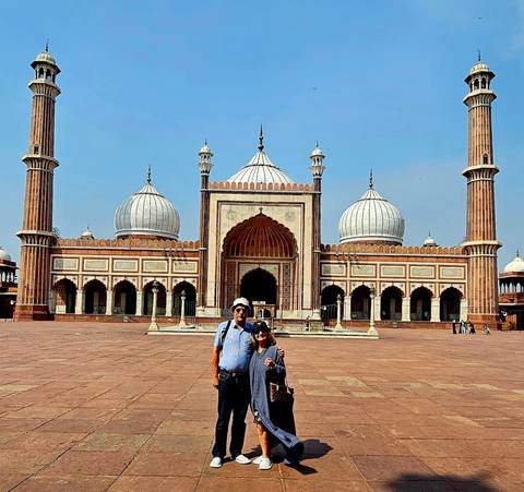 A couple poses in the vast courtyard before the domed Jama Masjid in Delhi under a clear sky.