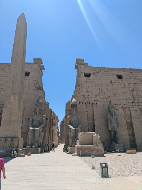 Statues of seated pharaohs and an obelisk flank the monumental entrance of Luxor Temple.