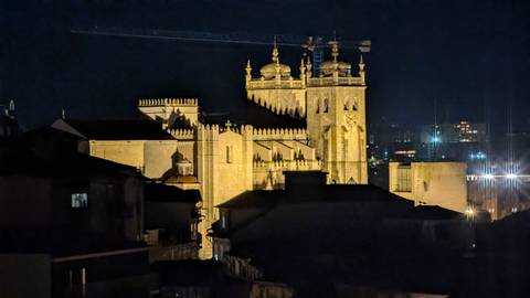 Night view of Porto Cathedral illuminated above dark rooftops with city lights in background.