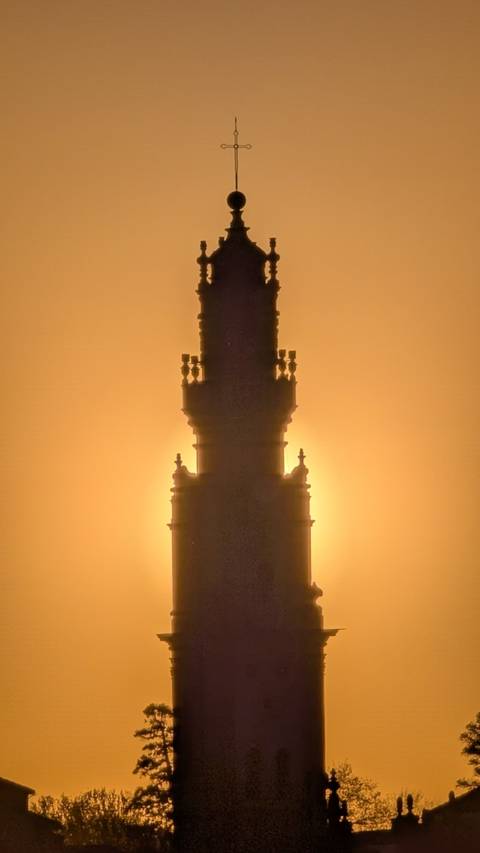 Silhouette of Clérigos Tower standing against a glowing orange sunrise sky.
