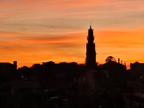 Orange dawn sky silhouettes Porto skyline with Clérigos Tower and historic rooftops.