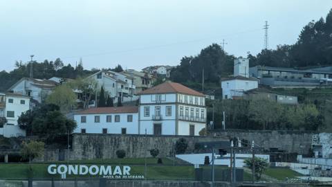 Riverside townscape of Gondomar with hillside houses and large welcome sign in early light.