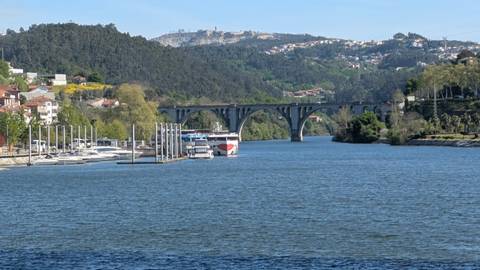 Arched stone bridge spanning the Douro River with cruise boats and forested hills beyond.