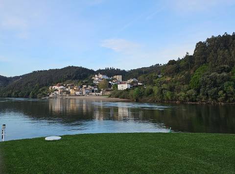 Small Portuguese village reflecting on calm river waters against forested hills.