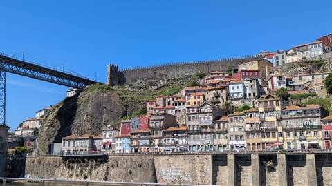 Colorful Ribeira district houses stacked on hillside beside steel bridge under bright blue sky.