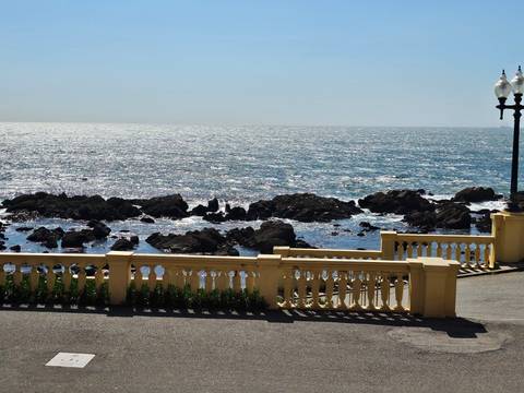 Sunny seaside view with crashing waves and rocky shoreline seen beyond a yellow balustrade promenade.