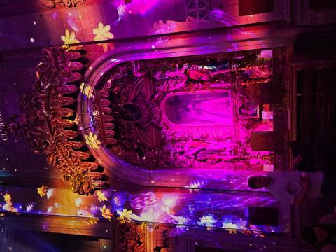 Vibrantly lit baroque altar with colourful projection effects inside a dim church interior.