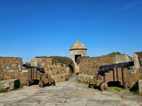 Stone fort entrance flanked by historic black cannons beneath a bright blue sky.