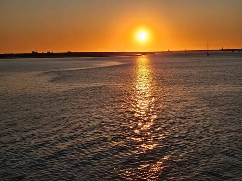 Golden sun setting over calm coastal waters leaving a shimmering reflection path.