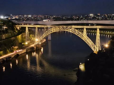 Illuminated metal arch railway bridge spans the Douro River against the night skyline.