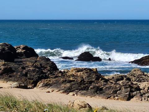 Powerful ocean waves crash against dark coastal rocks under a bright sky.