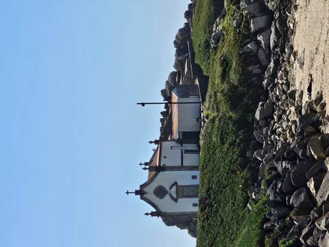 Small white coastal chapel perched on grassy rocks beside the sea.