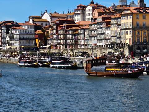 Bustling Ribeira waterfront in Porto with colourful facades and tourist boats moored along the Douro.