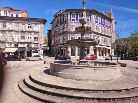 Historic town square with stone fountain, classic Portuguese buildings and parked cars.