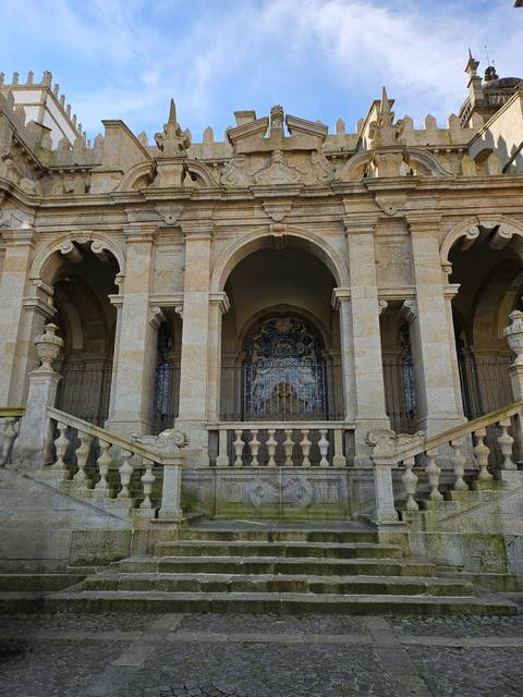 Grand stone arcade with staircases and hidden azulejo panel behind iron railings.