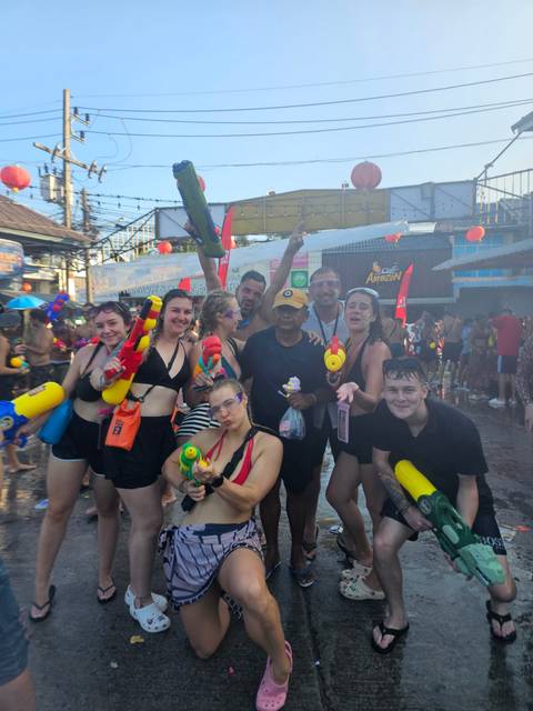 Crowded street scene of Songkran festival with smiling travellers wielding colorful water guns.