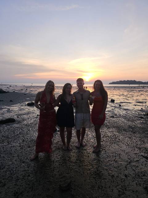 Four friends holding cocktails on a tidal flat during a colorful sunset.