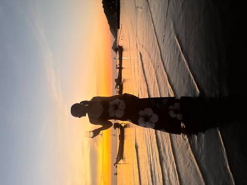 Silhouette of a woman holding a wine glass while standing ankle-deep in the sea during a vivid sunset.