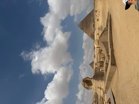 Iconic view of the Sphinx with pyramids rising behind under a blue sky dotted with clouds.