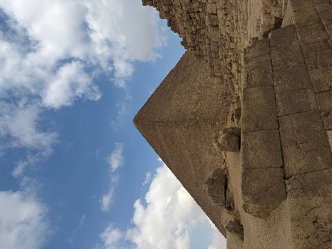 Close-up perspective of a pyramid against a dynamic sky, showing ancient stone blocks.