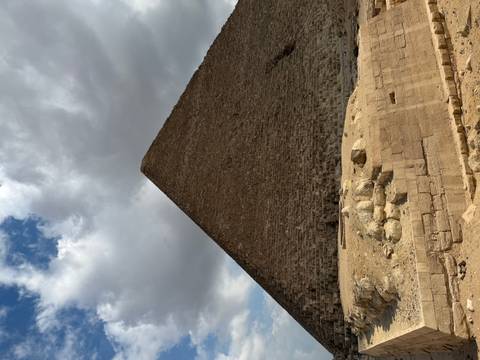 Side profile of a pyramid beneath dramatic clouds above a sandy plateau.