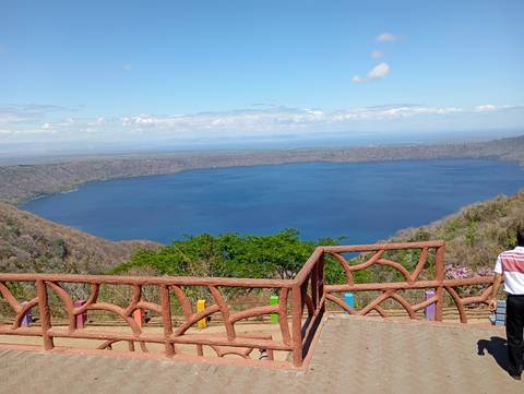 Blue volcanic crater lake viewed from a colorful wooden lookout railing on a sunny day