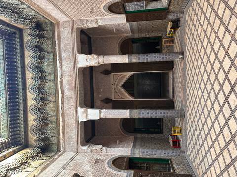 Ornate courtyard with mosaic tilework and carved arches inside a historic Moroccan madrasa