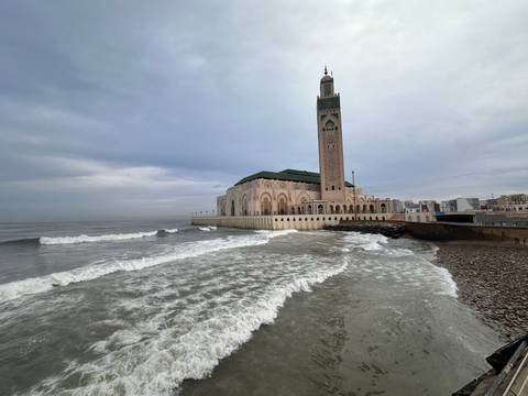 Hassan II Mosque standing over crashing Atlantic waves under an overcast sky