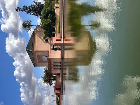 Menara Gardens pavilion reflected in a tranquil pool with palm trees and clouds