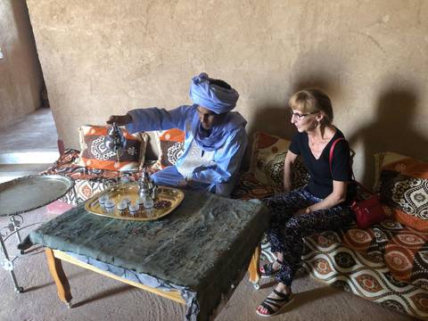 Local Berber host demonstrating products to a seated traveller inside an adobe room