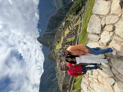 Family poses at scenic overlook of Machu Picchu ruins with Huayna Picchu peak behind.