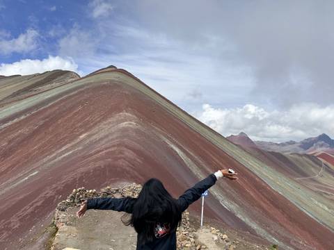 Traveller spreads arms wide while admiring the dramatic ridge of Rainbow Mountain.