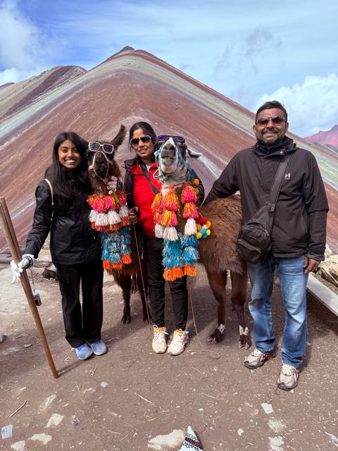 Travellers pose with festively decorated llamas against the backdrop of Rainbow Mountain.