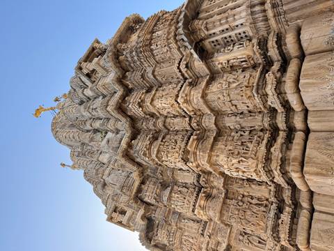 Upward view of intricately carved stone temple tower against a clear blue sky.