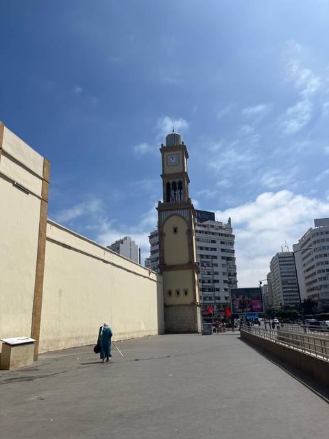 Slim historic clock tower rises beside modern office blocks under bright blue sky.