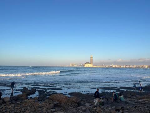 Wide coastal view with Atlantic waves and iconic Hassan II Mosque rising in background.