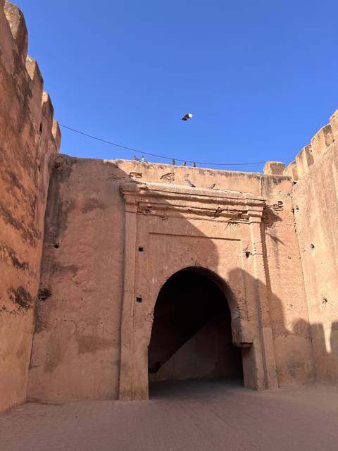 Weathered adobe gateway with pigeons perched atop against vivid blue sky.