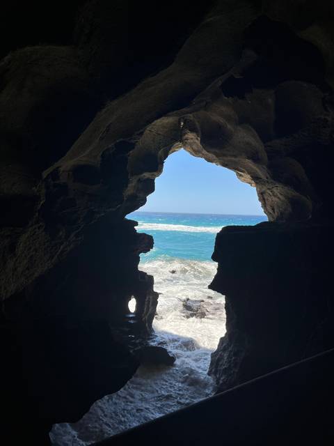 View from inside a seaside cave framing turquoise waves and bright horizon.